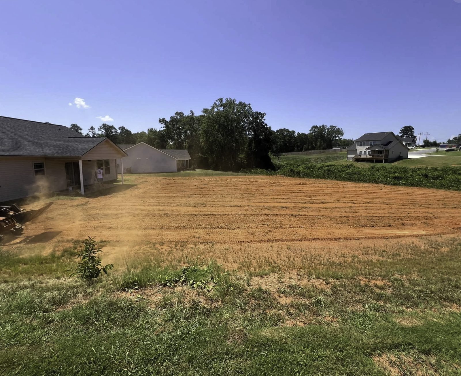 Large residential lot graded and prepped for landscaping, house and skid steer visible