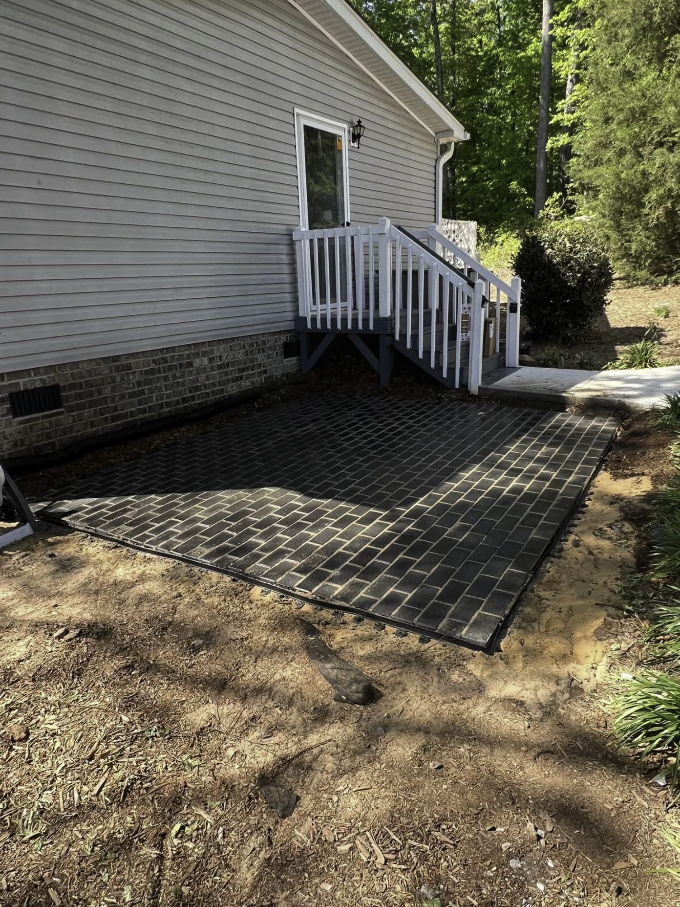 New dark paver patio installed behind a house, next to a white deck staircase