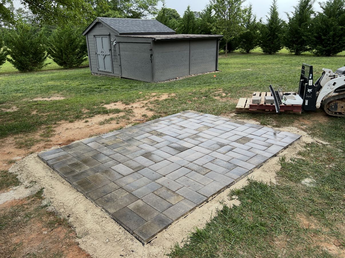 New paver pad laid on a sand base in a backyard near a storage shed