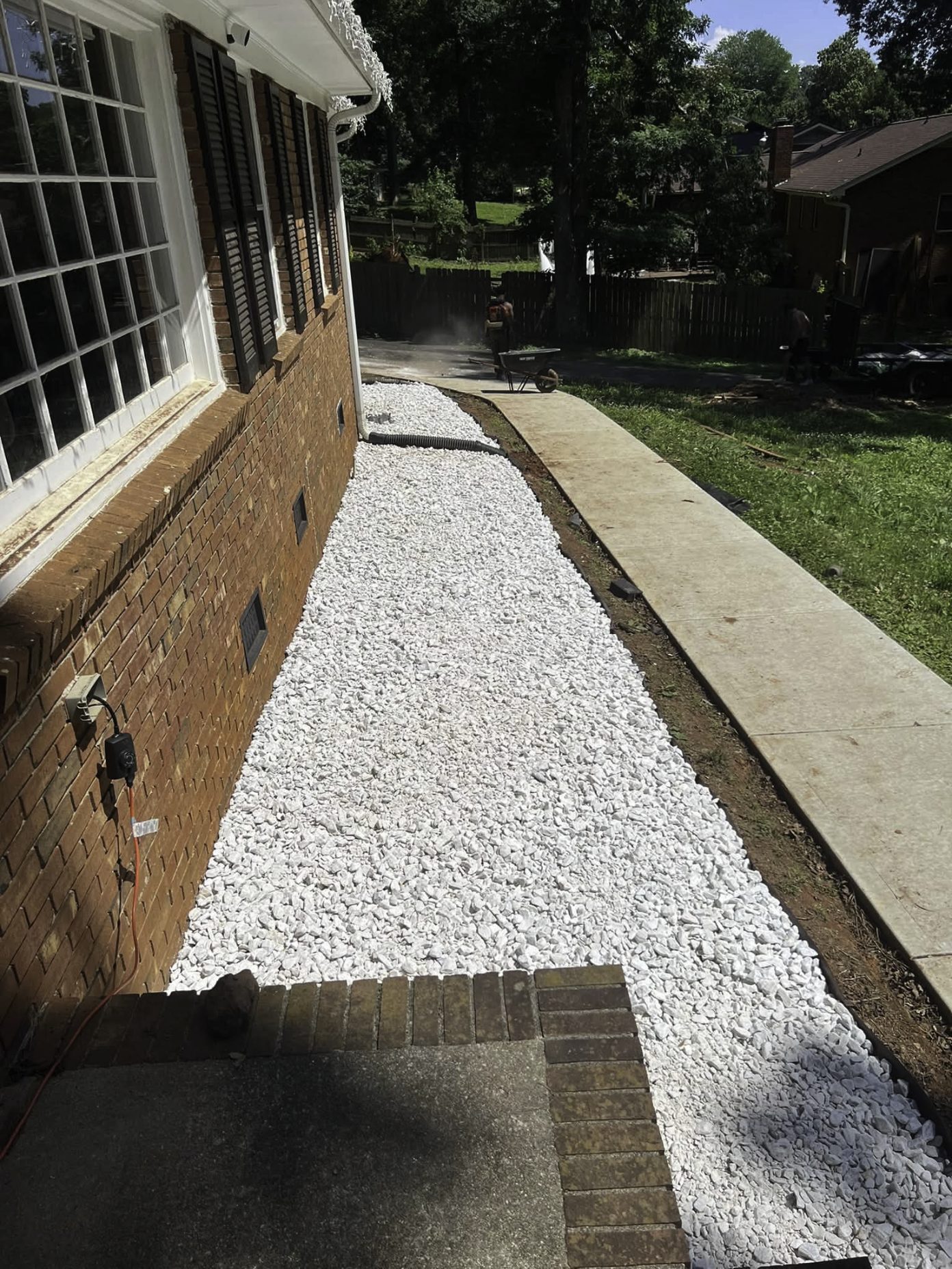 White stone drainage walkway installed along a brick house foundation, next to a new concrete sidewalk